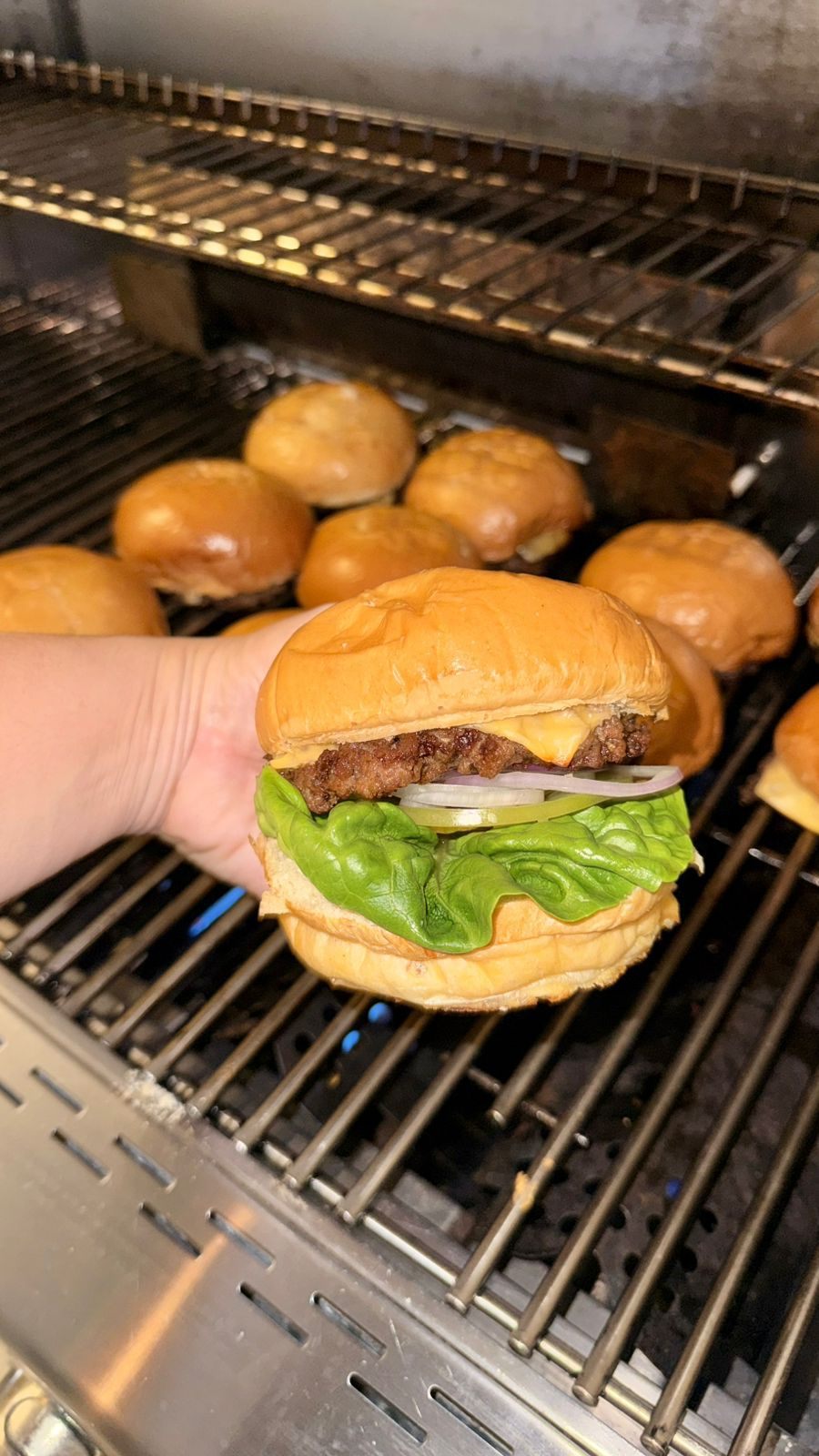 Hamburguesa terminada sobre la parrilla, con los panes calent&aacute;ndose atr&aacute;s