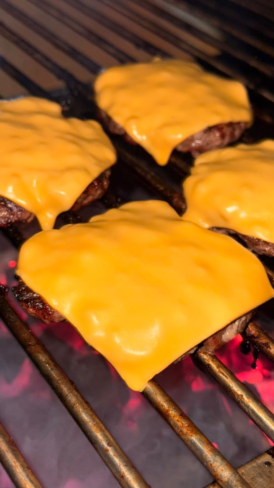 Queso cheddar derriti&eacute;ndose sobre las carnes en la parrilla